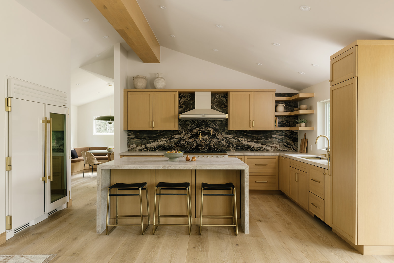 West Aspen Retreat kitchen with oak cabinetry, a stone backsplash, and an island with three counter stools.